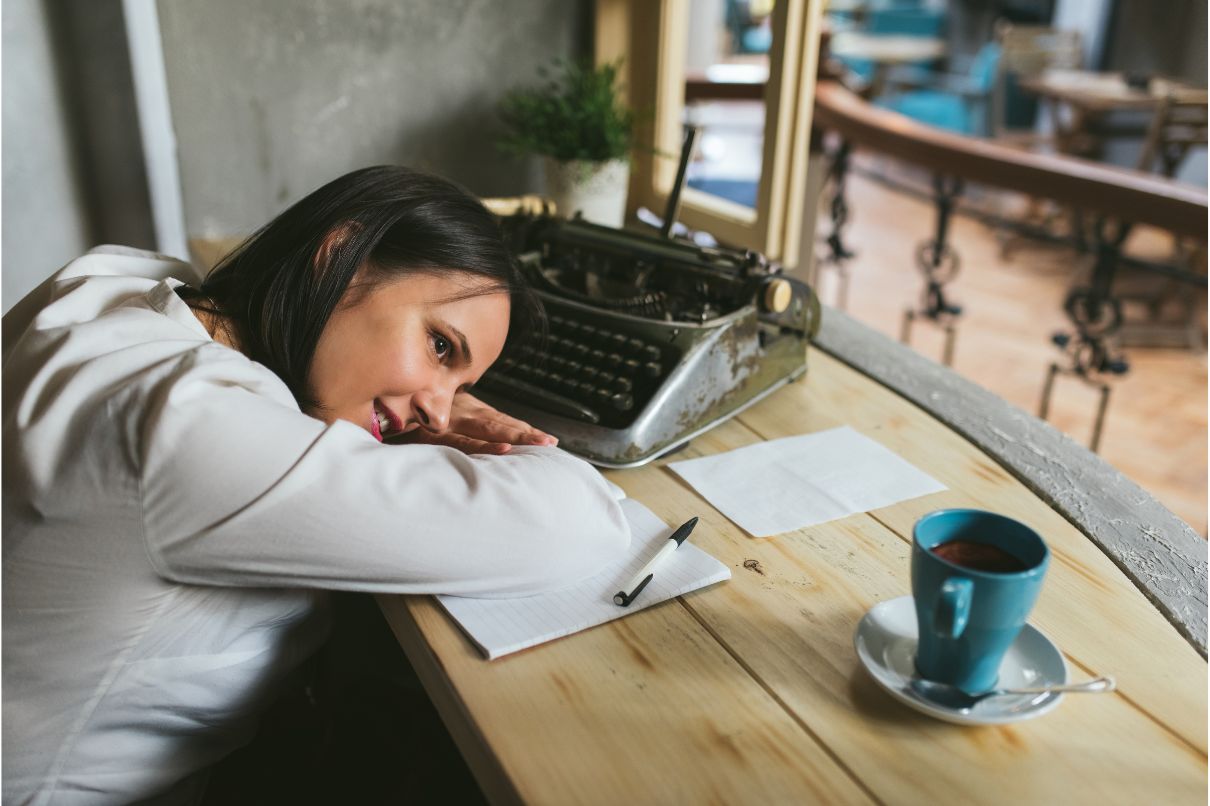 A woman sleeping on a desk with a cup of coffee, symbolizing exhaustion and the need for caffeine.