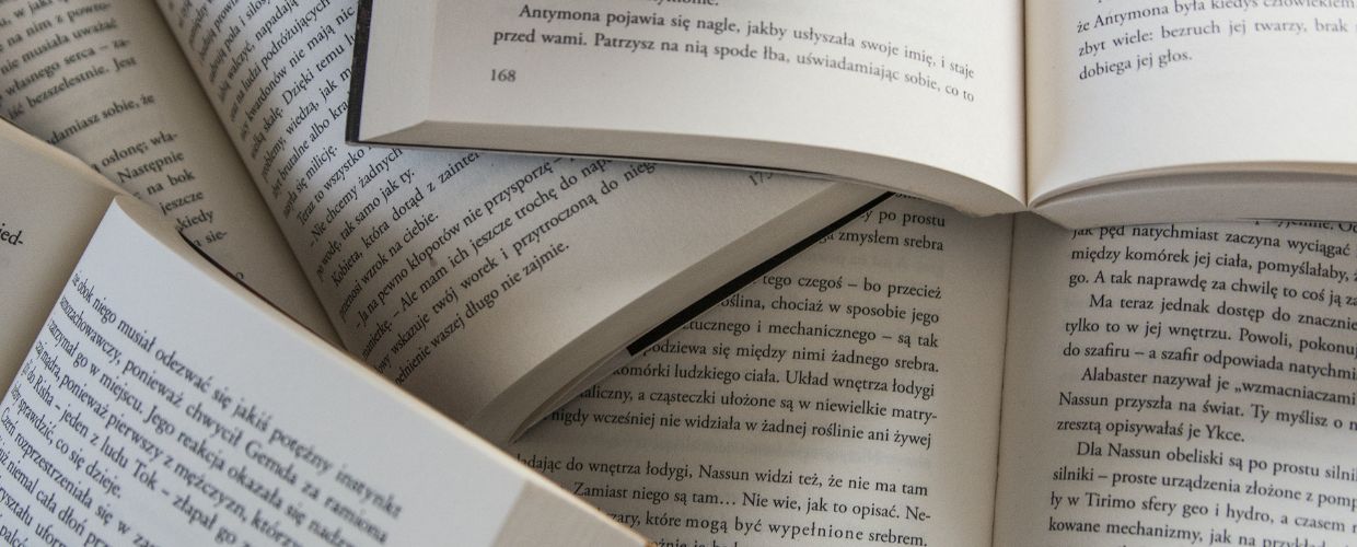 A stack of open books arranged on a wooden table, showcasing various pages and colorful covers.