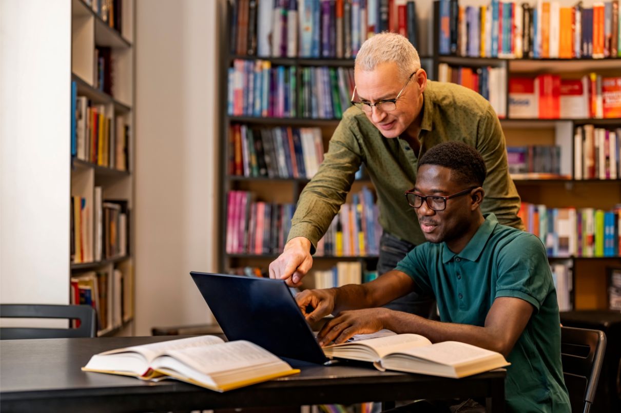 Two men collaborating on a laptop in a library, engrossed in their work