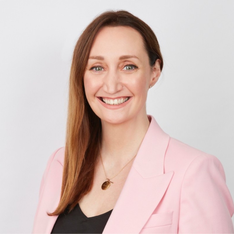 A woman wearing a pink blazer over a black top, exuding confidence and style in a professional setting.